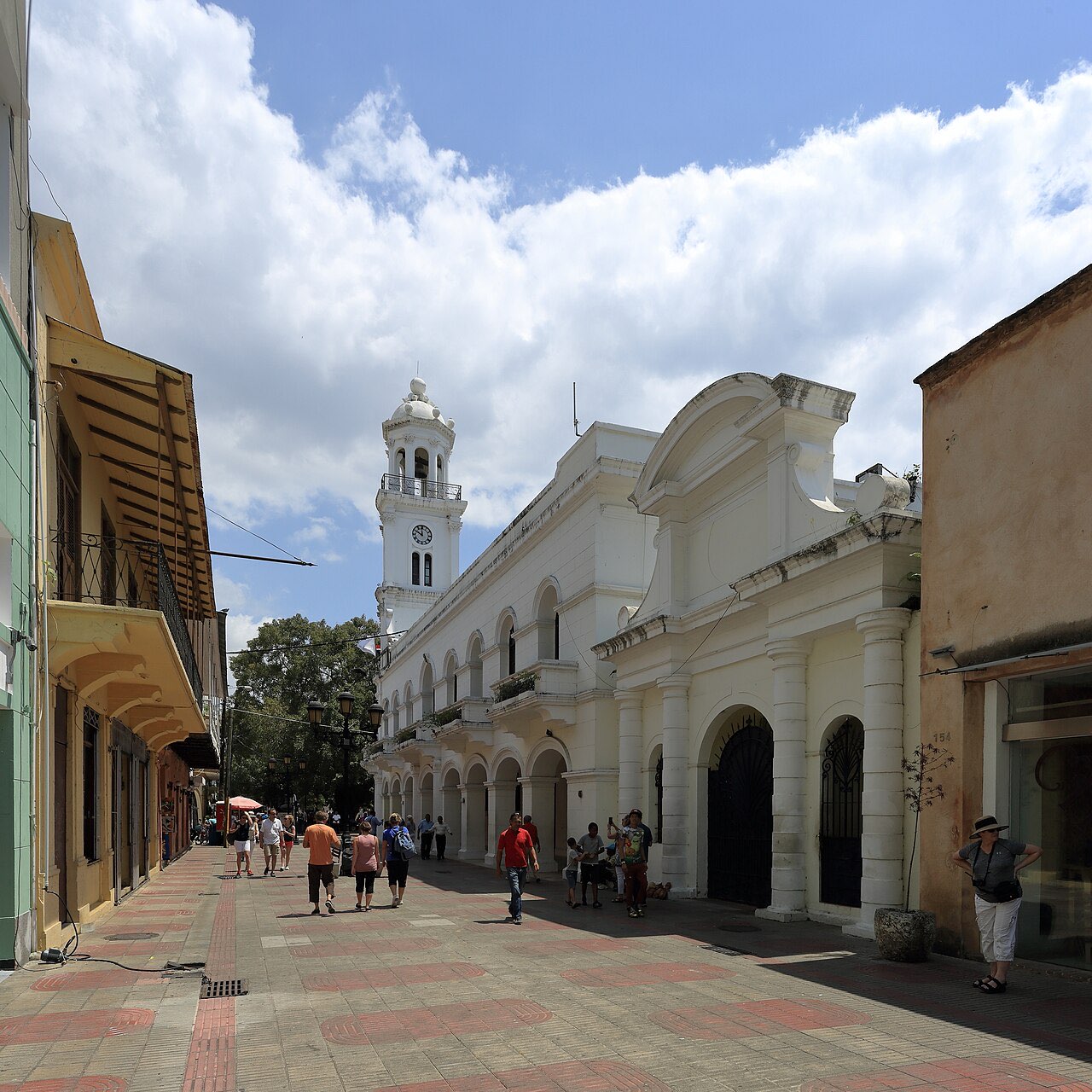 Pedestrians walking along Calle El Conde in Santo Domingo's Zona Colonial with the white Palacio Consistorial and clock tower ahead