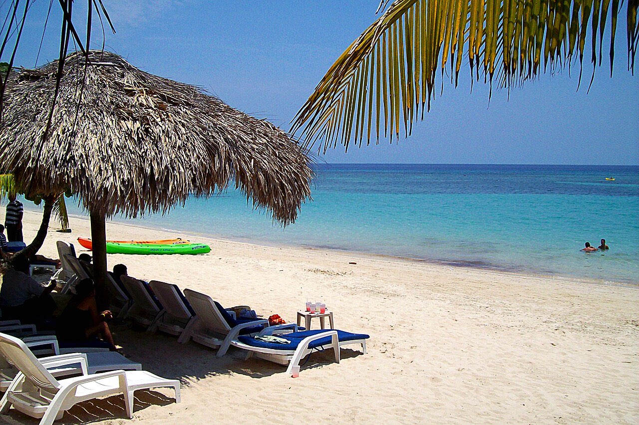 A white-sand beach on Roatan with thatched sun umbrellas, loungers and calm turquoise water