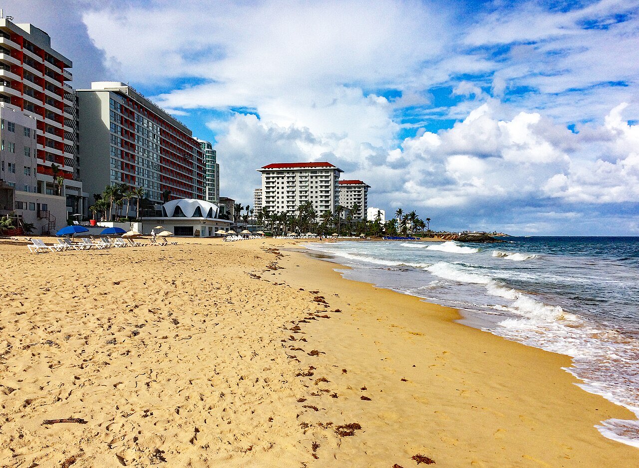 Breaking waves on a sandy beach at Condado in San Juan with high-rise hotels along the shoreline behind
