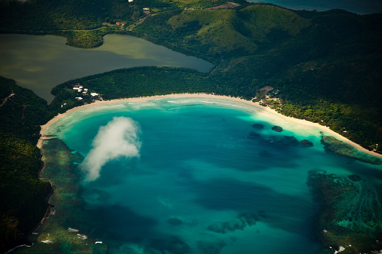 Aerial view of a curving white-sand bay with turquoise water and forested hills at Flamenco Beach on Culebra