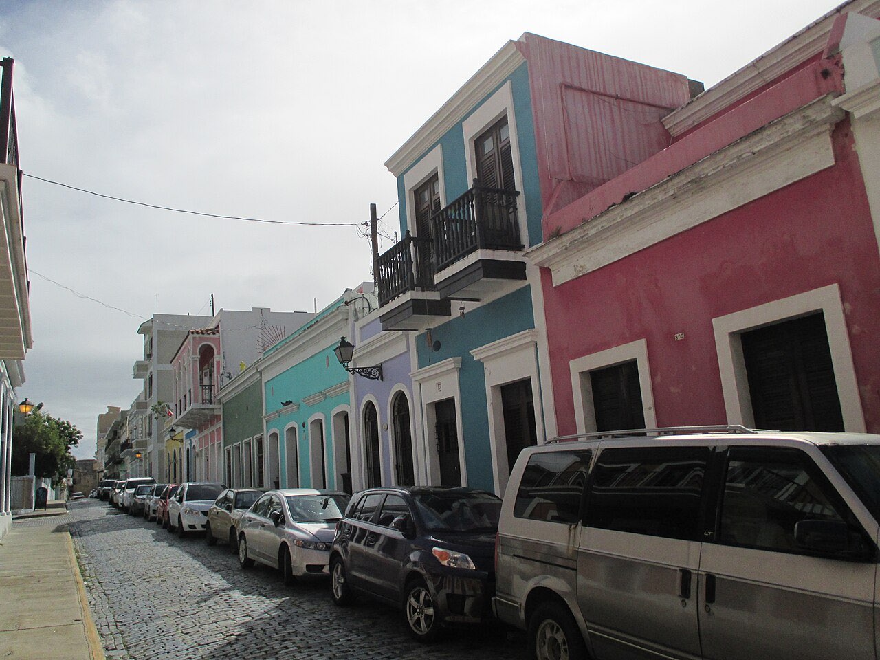 A cobbled street in Old San Juan lined with pink, blue and pastel colonial buildings with balconies and parked cars