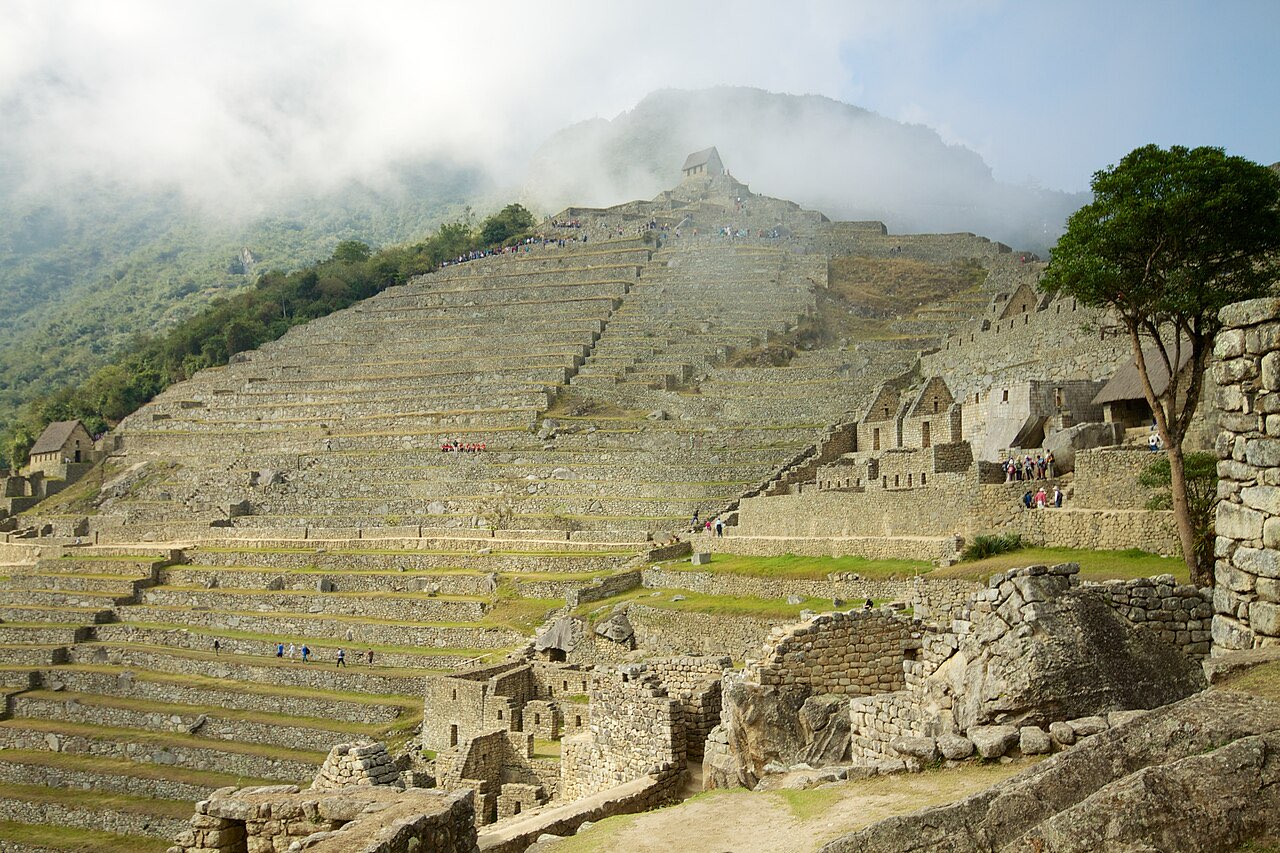 Wide stepped agricultural terraces climbing a misty hillside above the ruins at Machu Picchu