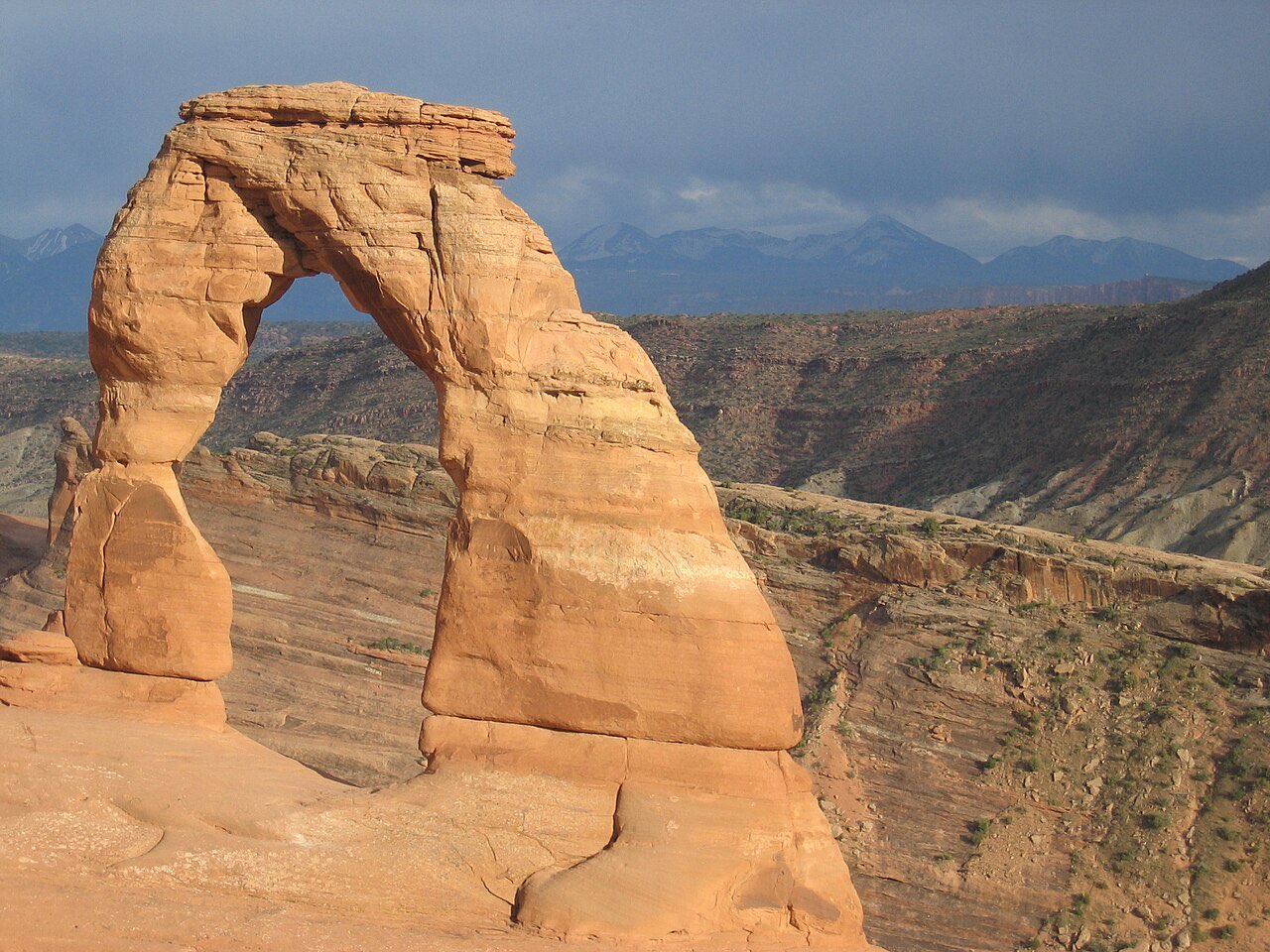Delicate Arch standing alone on slickrock in Arches National Park with distant mountains behind