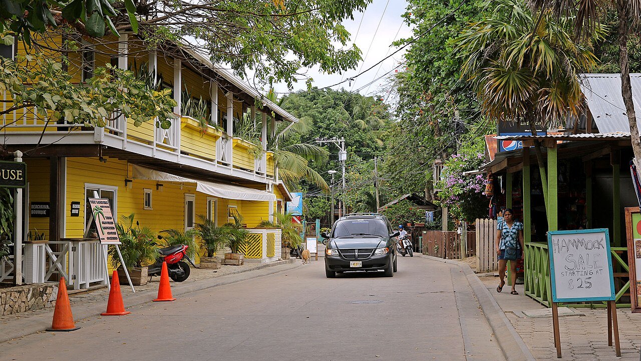 A narrow street in West End, Roatan, lined with wooden buildings, a yellow two-storey guesthouse and a hand-painted sign